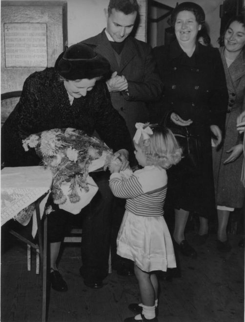 Jenny Brown presenting a bouquet 1952. This picture also shows the commemorative plaque celebrating the opening of the village school in 1874. | Phyllis Owens
